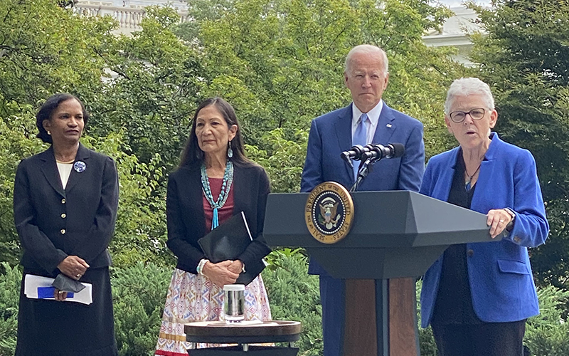 woman standing at a podium with Joe Biden and two other women standing behind