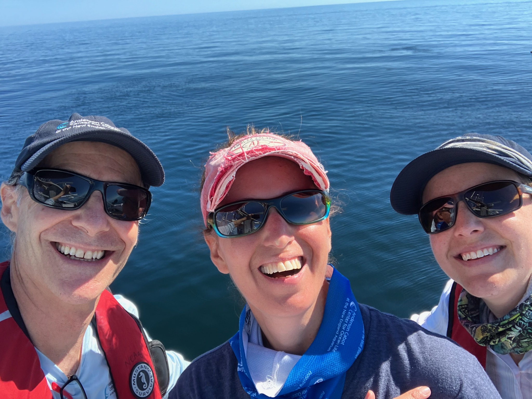 three smiling people wearing sunglasses outside on a boat