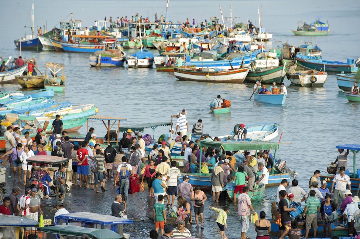 People walking on a seaside promenade alongside several boats