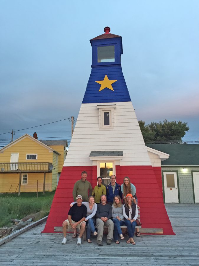 Nine people posing in front of a small lighthouse