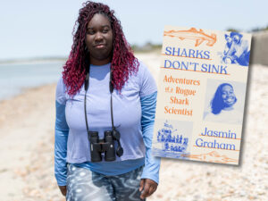 Jasmin Graham walks along a beach with the cover of her book Sharks Don't Sink