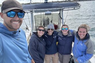 A group selfie of five people on a boat. Dr. Knotek is in front taking the photo and wearing sunglasses