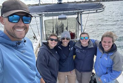 A group selfie of five people on a boat. Dr. Knotek is in front taking the photo and wearing sunglasses