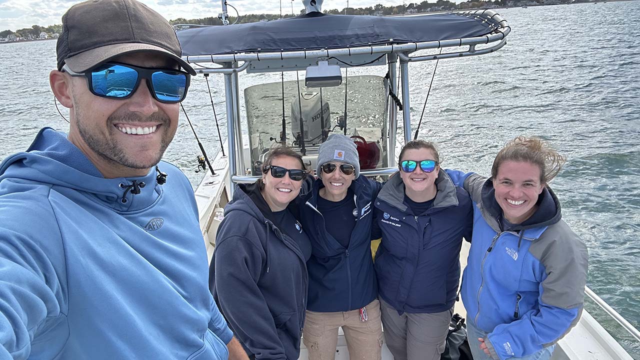 A group selfie of five people on a boat. Dr. Knotek is in front taking the photo and wearing sunglasses