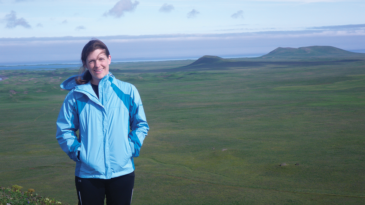 Patty in a blue coat with green landscape and the ocean behind her